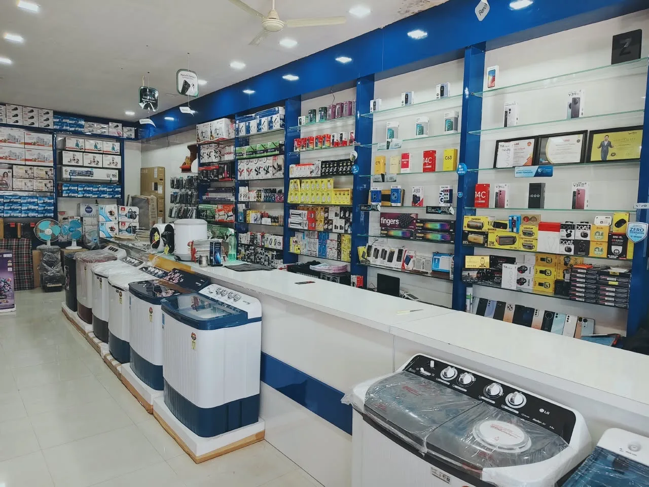 Mobile phones and accessories on the blue and white display shelves at Shivam Mobile & Electronics